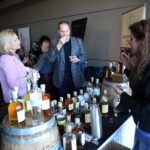 a group of people standing next to a bottle of wine